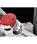 Hands holding sander with red Hook And Lock ROS Sanding Discs For Wood Metal And Plastics 5 Inch 60 Grit Coarse Ceramic Blend