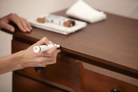 Fire DIY Wood Furniture Scratch Repair Kit With Three Touch Up Markers And Wax Filler Sticks For No Sweat Scuff Control On Cabinets And Table Surfaces In Brown being applied to a wooden table.
