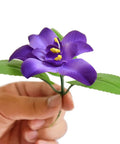 Hand holding artificial purple flower component of Dope Expandable Faux Ivy Privacy Screen With Artificial Flowers And Greenery
