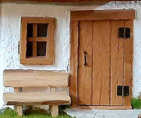 Miniature dollhouse with wooden door featuring brass hinges, matching window and bench, showcasing tiny craftsmanship details.