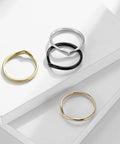 Four simple thin rings in silver, black, gold, and rose gold, stacked on white background