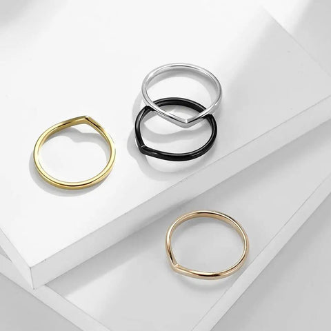 Four simple thin rings in silver, black, gold, and rose gold, stacked on white background