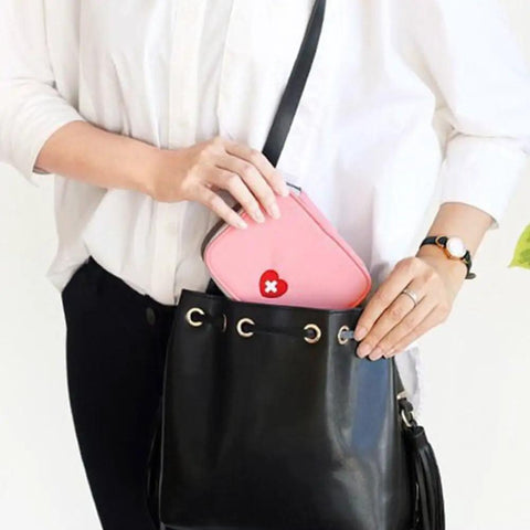Person placing Pink Mini Outdoor First Aid Kit Bag For Travel And Everyday Use into black handbag