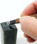 Hand using chisel on soapstone from 18-Piece Stone Carving Kit With Manganese Steel Chisels, Mini Vise Clamp, Beeswax, And Oxford Storage Bag