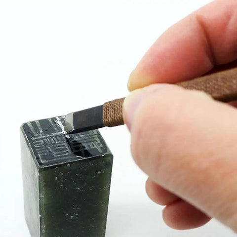 Hand using chisel on soapstone from 18-Piece Stone Carving Kit With Manganese Steel Chisels, Mini Vise Clamp, Beeswax, And Oxford Storage Bag