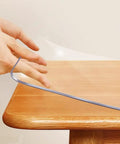 Hand lifting Clear 14x24 Inch Desk Blotter Mat Transparent PVC Table Protector Pad For Small Offices on a wooden desktop.