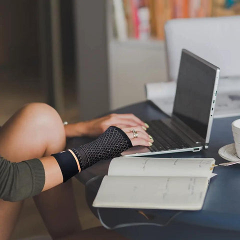 Person wearing Copper Wrist Compression Sleeve 1 Pair For Pain Relief And Support, Helps Arthritis Tendonitis Carpal Tunnel Sprains, working on laptop