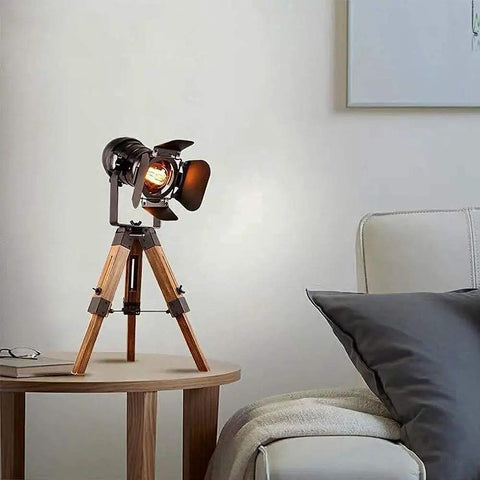 Tripod Floor Lamp With Industrial Vintage Vibe, Metal And Wood Finish, Nautical Cinema Style, on a side table in a living room.