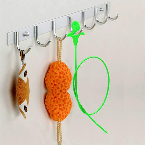 Flexible 3D Drain Snake With Soft Barbed Wand For Hair And Debris Removal in green, hanging on a hook, visible with sponges.
