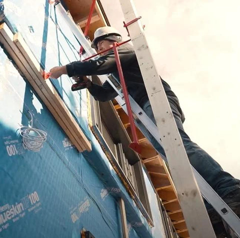 Metaltech pump jack brace 2201 installed on blue exterior wall with a worker on a ladder.