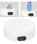 Motorized 360 Degree Rotating Turntable Stand For Jewelry Photography displaying ring and smartphone on white base.