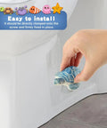 Hand placing a blue turtle onto a toilet for installation, showcasing Totally Adorable Turtle Toilet Bolt Covers, Ceramic Screw Caps.