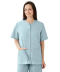 Women Snap Front Jewel Neck Scrub Top Double Cargo Pockets Misty Medium Cotton Polyester Blend Top in light blue worn by a smiling model.