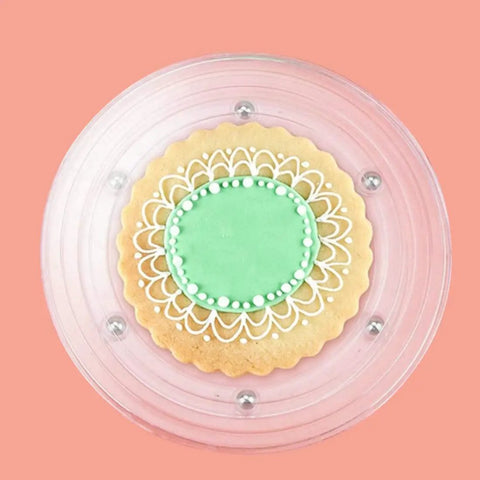 Level Up Your Baking Game With This Nifty 8 Inch Acrylic Cookie Decorating Turntable Kit Featuring Six Sturdy Brushes And Six Precision Scribe Tools For Flawless Icing And Sugar Craft Designs, featuring a decorated cookie on a clear turntable.