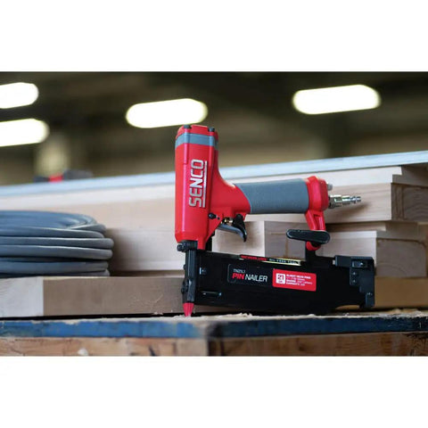 Pro Grade Pneumatic Pin Nailer For Cabinet Trim And Fine Woodworking Ships Ready Using Twenty One Gauge Straight Collated Pins From Half Inch To Two Inches, positioned on wood with hose in background.
