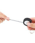 Retractable tape in hand showing measuring markings, part of Two Piece Measuring Wheel And Retractable Tape Featuring Cm And Foot Dial And Heavy Duty Click Lock For Slick Fence Lines Tire Gauges And Quick Site Markouts That Handle Hard Labor Like A Champ And Ride Easy In Your Trunk.