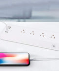 Totally Smooth Smart Power Strip With Four Wall Outlets And Four USB Charging Ports, white design, charging phone visible.