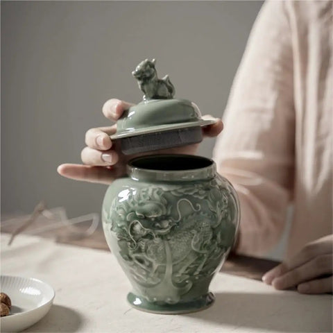 Top Tier Ceramic Airtight Tea Canisters For Loose Tea Leaves And Coffee Beans Hand Embossed Celadon Kirin Design, shown with lid being removed.