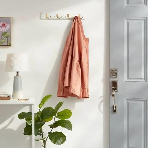 Swoop Up Fresh Wall Mounted Coat And Hat Rack Featuring Four Sleek Gold Dual Hooks On A Crisp White Base with a jacket hanging.