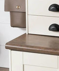 White furniture corner with dark handles and wooden top, against a white shiplap wall with flowers.