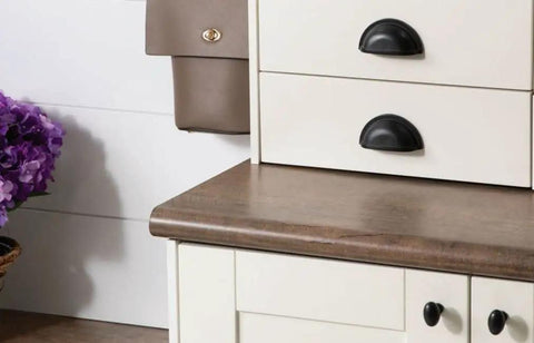 White furniture corner with dark handles and wooden top, against a white shiplap wall with flowers.