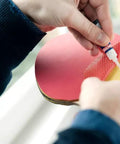Loctite Super Glue Liquid close-up: applying clear adhesive to a red circular craft piece with yellow underside.