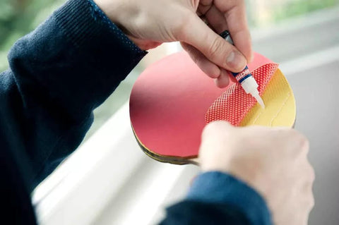 Loctite Super Glue Liquid close-up: applying clear adhesive to a red circular craft piece with yellow underside.