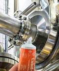 Haynes Lubri-Film Plus food-grade grease tube with orange label beside stainless steel industrial piping