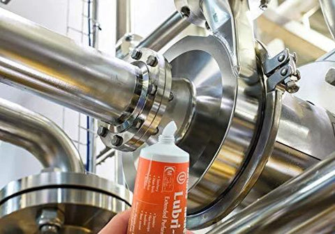 Haynes Lubri-Film Plus food-grade grease tube with orange label beside stainless steel industrial piping