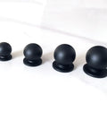 Four solid brass matte black ball knobs in varying sizes for cabinets and drawers on white surface.