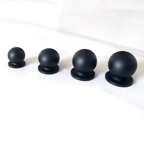 Four solid brass matte black ball knobs in varying sizes for cabinets and drawers on white surface.