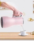 Grab And Go Kickass Vacuum Insulated Travel Thermos With Secure Silicone Lid pouring into a cup on a wooden table.