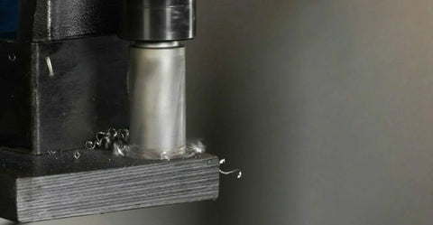 Close-up of 5/8 x 1 in high-speed steel annular cutter in drill press chuck, cutting metal with chips