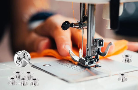 Sewing machine bobbins and bobbin case on white surface with orange fabric under the presser foot