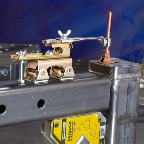 Front view of brass-toned Deluxe Magnetic Grasshopper welding finger with copper spindle and magnetic V-Pad base on steel workbench