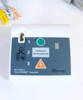 Front view of an AED training unit with blue control panel, green button, 1–4 step indicators, and training-only label