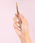 Hand holding brush from 16 Fl Oz Liquid Monomer For Nail Extensions With 100 Percent Kolinsky Size 10 Brush Starter Duo Includes 6 Fl Oz Monomer And Pro Grade Brush For Smooth Long Lasting Salon Worthy Nail Applications