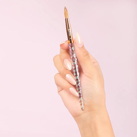 Hand holding brush from 16 Fl Oz Liquid Monomer For Nail Extensions With 100 Percent Kolinsky Size 10 Brush Starter Duo Includes 6 Fl Oz Monomer And Pro Grade Brush For Smooth Long Lasting Salon Worthy Nail Applications