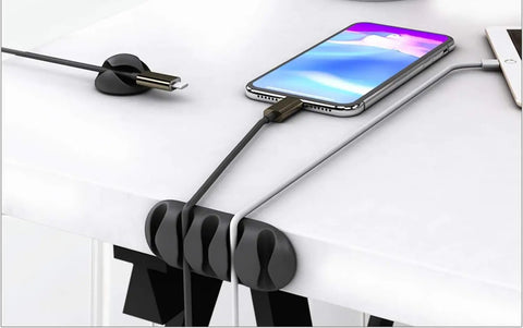 Black cable clips holding charging cables on a white desk, part of 16 Pack White Self Adhesive Cable Clips For Desk And Nightstand Cable Management.