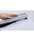 Hand using Rock Solid 3 Hole Punch for office and home use with 12 sheet capacity, heavy duty metal construction, rubber base, sleek silver finish.