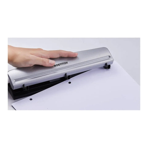 Hand using Rock Solid 3 Hole Punch for office and home use with 12 sheet capacity, heavy duty metal construction, rubber base, sleek silver finish.