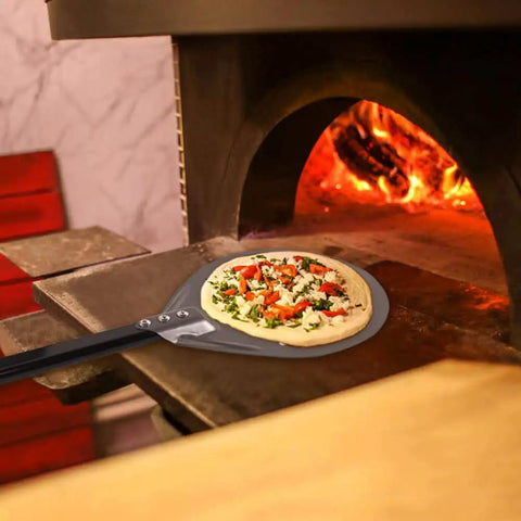 9 Inch Round Perforated Aluminum Pizza Peel With Detachable 40 Inch Handle Lightweight Yet Durable Pizza Turner For High Heat Ovens Outdoor Pizza Oven Accessories For Easy Slide And Turn Pro Grade shown with pizza in oven.