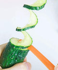 Green spiral slicer with orange handle in close-up slicing cucumber into spirals; manual kitchen gadget