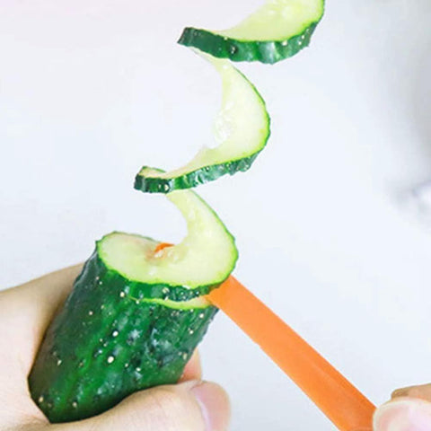 Green spiral slicer with orange handle in close-up slicing cucumber into spirals; manual kitchen gadget