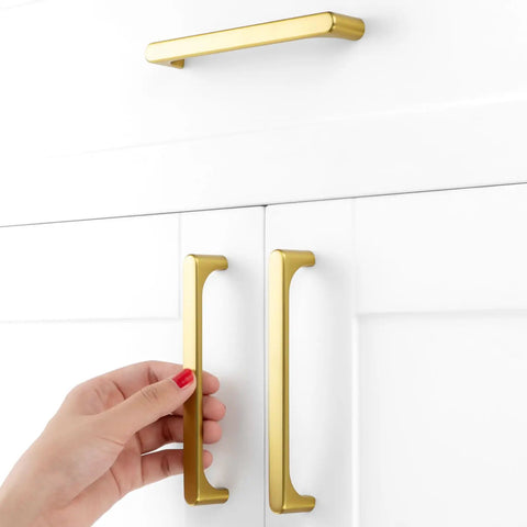 Hand reaching for Rock Solid Brushed Gold Cabinet Pulls Kitchen Handles 5 Inch 128mm Centers on white cabinetry.