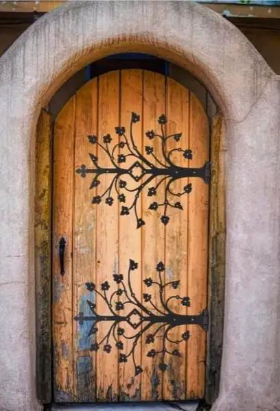 Kick Ass Wrought Iron Door Hinges With Glossy Black Powder Coating on decorative wooden door with tree design.