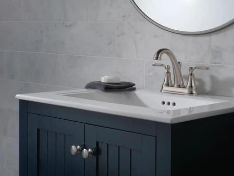 Woodhurst Centerset Brushed Nickel Dope Sleek Bathroom Faucet on white sink with navy cabinet and round mirror