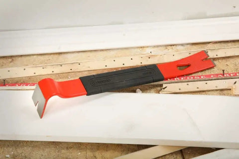 Red and black 15 Inch Flat Pry Bar with Grip for demolition, beveled nail slots, rust-resistant, on construction site.