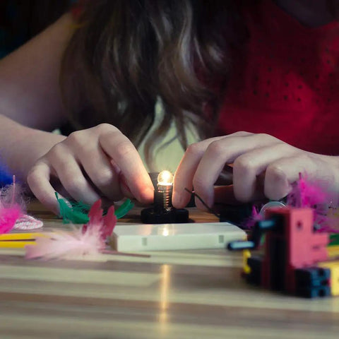 Child assembling Totally Hands On Electric Circuit Kit For Kids Diy STEM Learning Set with lit bulb on wooden table.