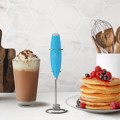 All Star Handheld Milk Frother Electric Drink Mixer Wand For Coffee Lattes Cappuccinos And Hot Cocoa Blends with blue handle next to coffee and pancakes.